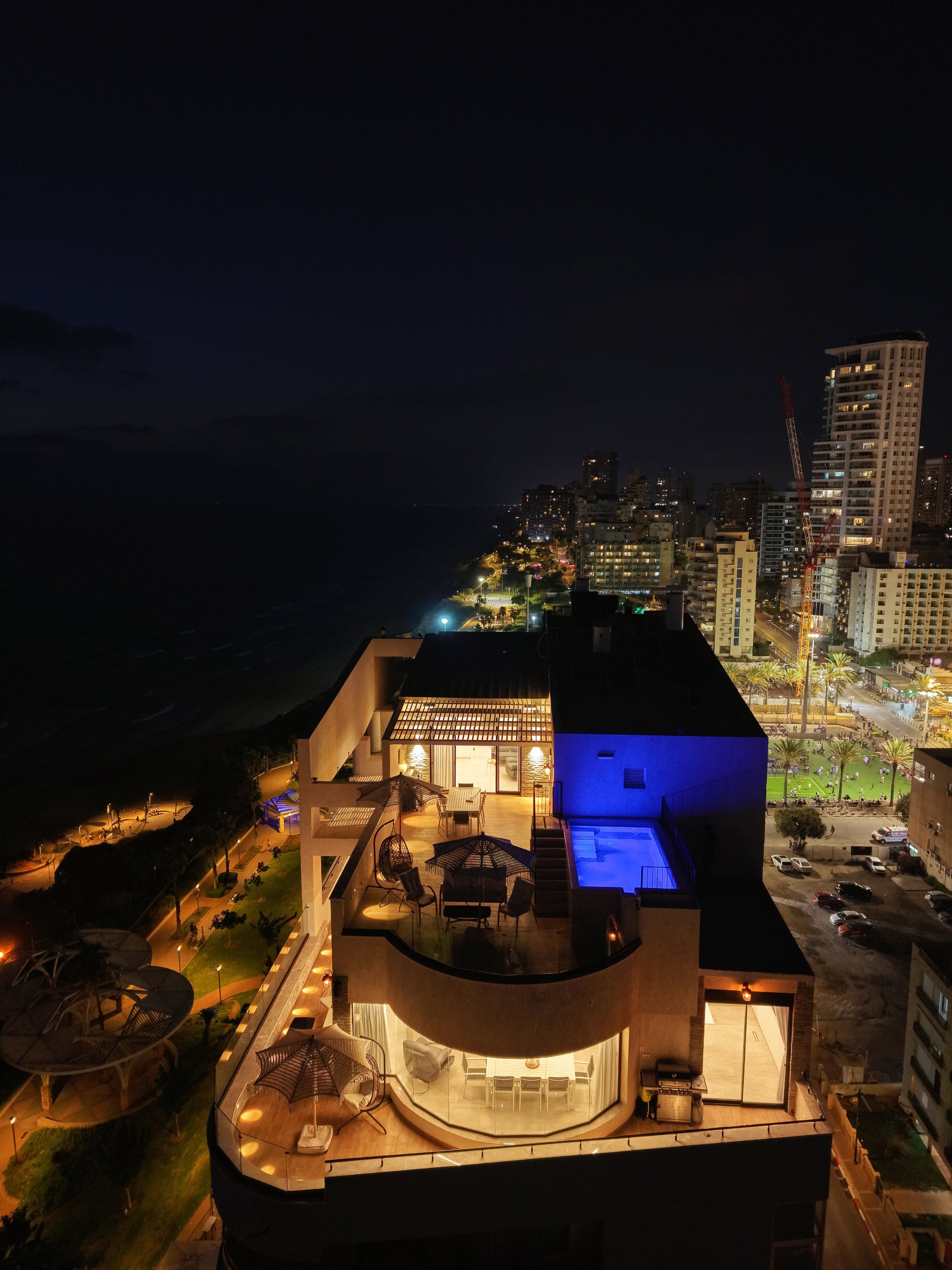 SEA VIEW בלילה מלמעלה: הבריכה המוארת על הגג, הטיילת וקו החוף של נתניה